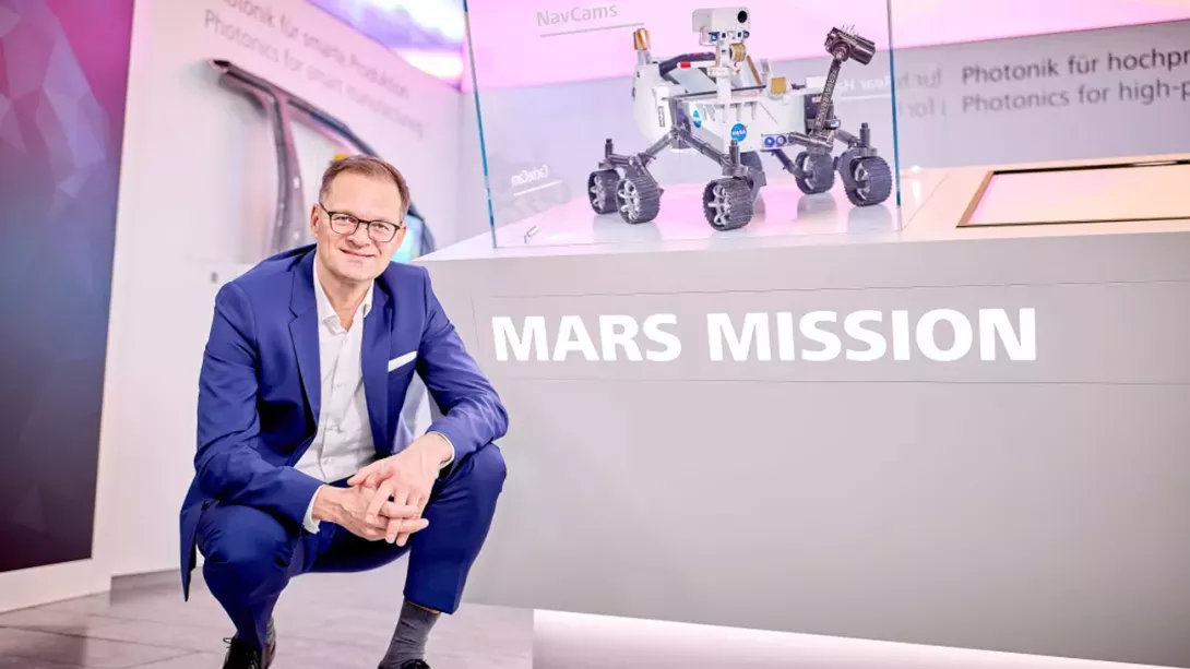 Man in suit kneels in front of a display case with a model of a Mars Mobile