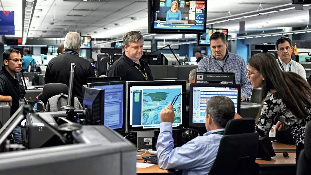 Several colleagues stand in the office around computers with weather data on the monitor