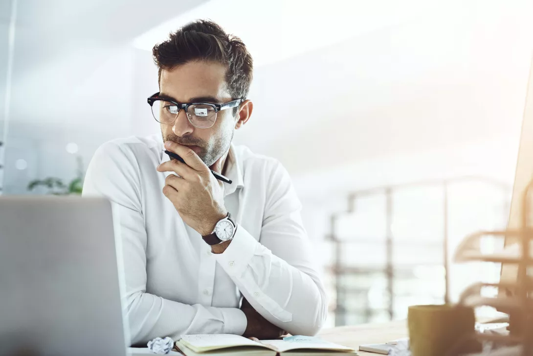 Mann am arbeiten schaut auf seinen Laptop und überlegt