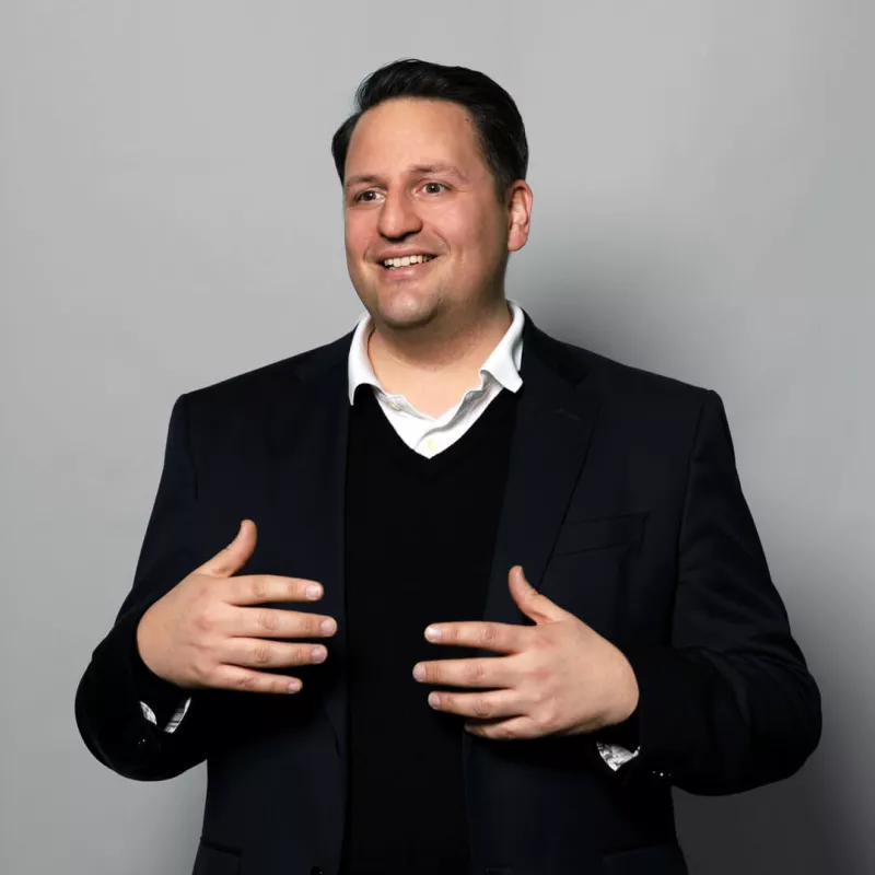 A consultant in a suit smiles at the camera against a grey background
