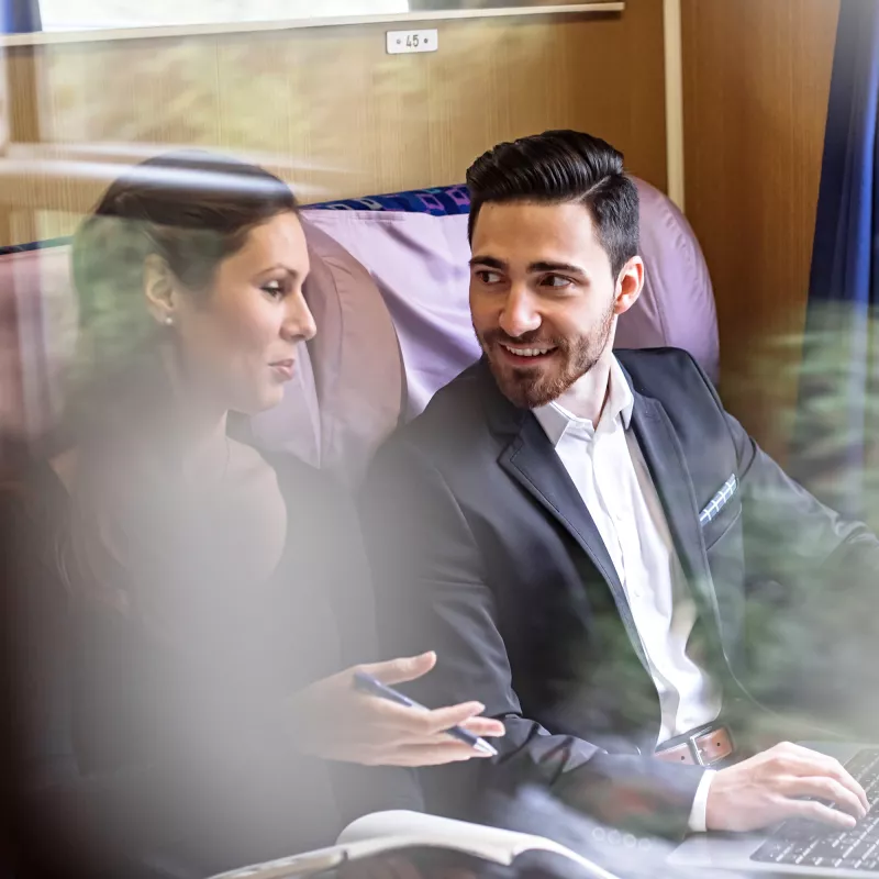 A woman and a man with a laptop are sitting in a train compartment and discussing
