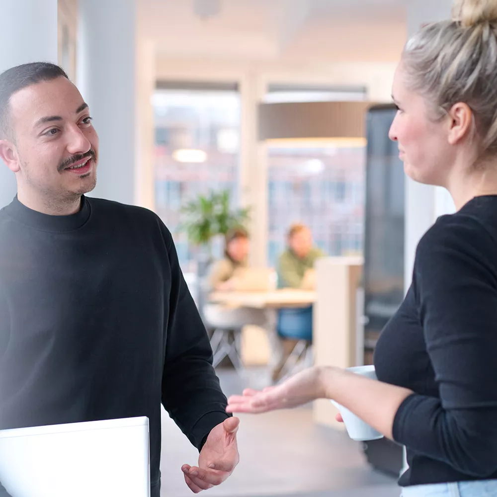 Consultant with laptop in arm discussing with a female colleague 