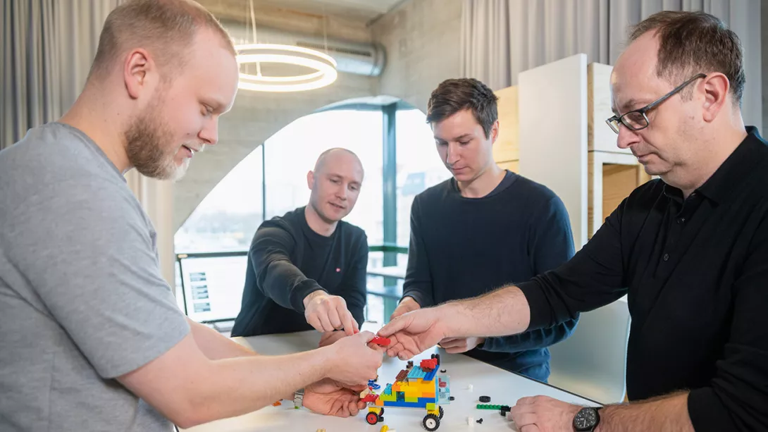 Four male colleagues assemble a car out of Lego in a creative office