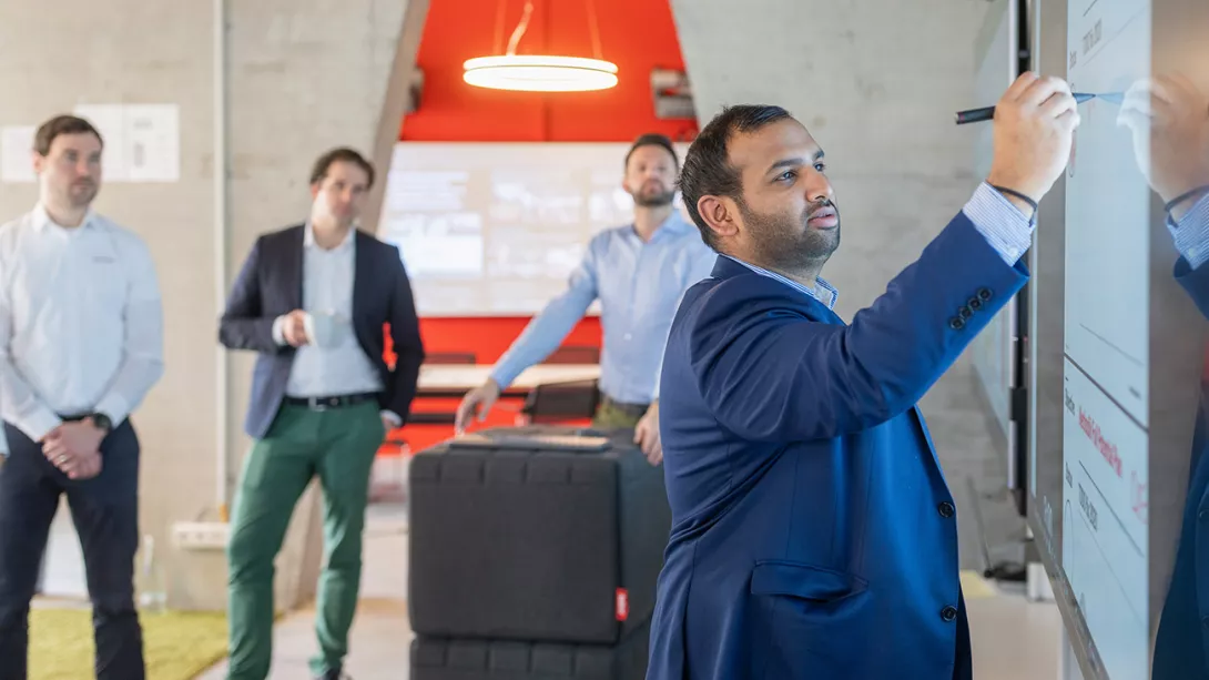 Man in suit writes something on a whiteboard, 3 colleagues watch him