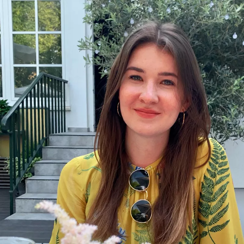 Portrait of a smiling junior consultant in front of a shrub in a courtyard