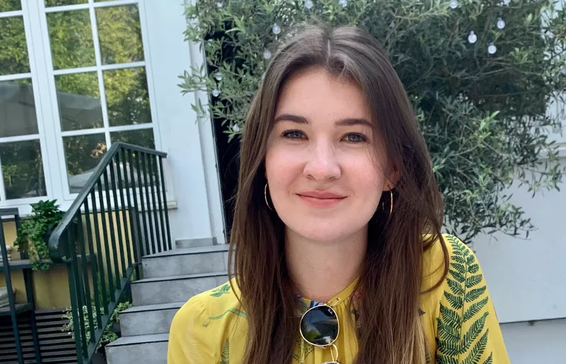 Portrait of a smiling junior consultant in front of a shrub in a courtyard
