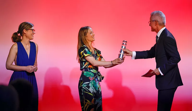 Drei Menschen stehen an der Bühne und bekommen  ein Preis