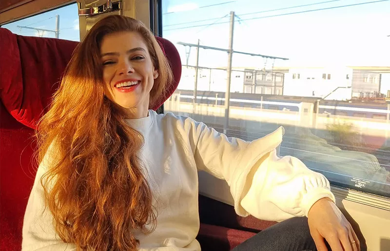 Young woman sitting in a train in front of the window through which the sun shines