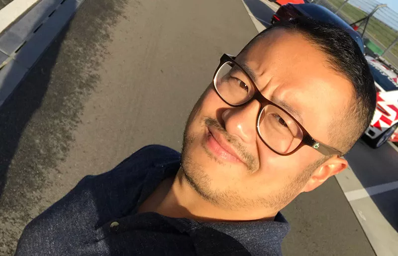 Close-up of a man standing in front of a racing car and smiling