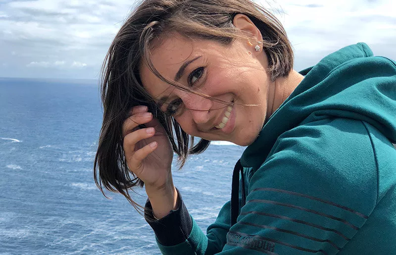 Woman laughing into the camera and in the background are sea and a cloudy sky