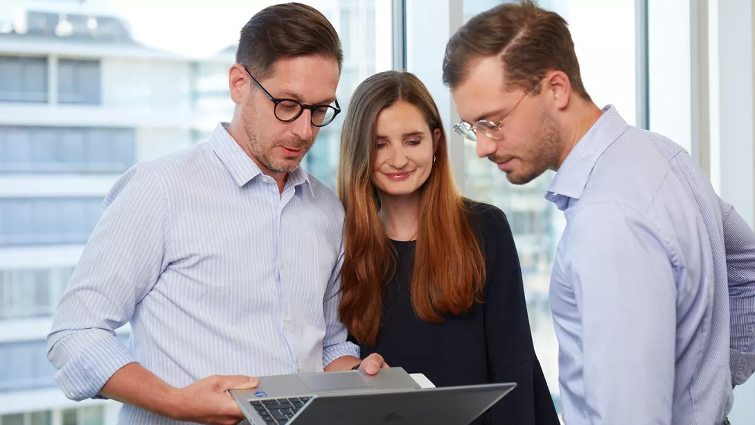 Two male and one female consultant in business outfits look at laptop