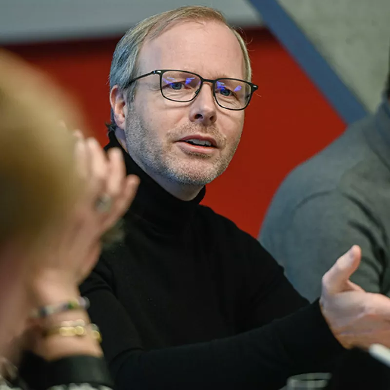 A man in a black jumper discusses with colleagues