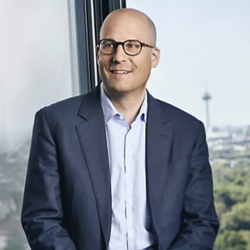 Man in a suit stands in front of a window in an office